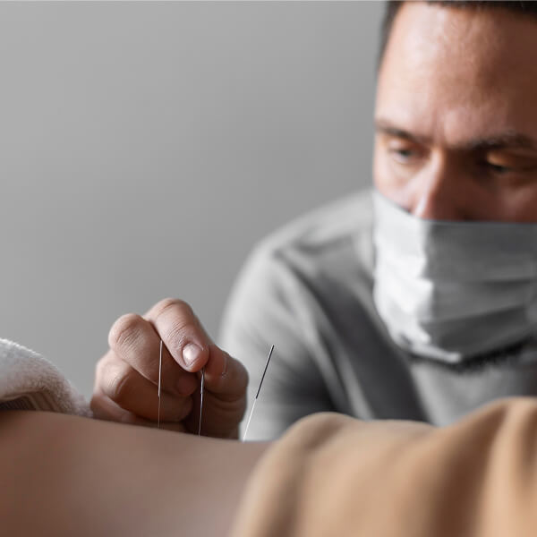 Un homme portant un masque facial reçoit un traitement d'acupuncture.